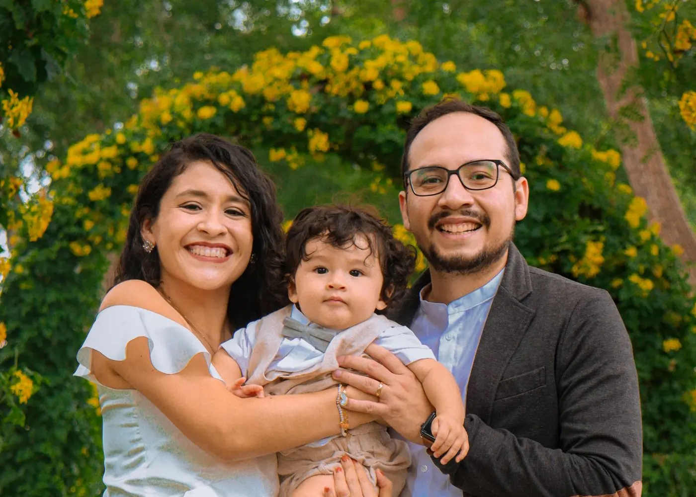 A smiling couple holding their child in a garden